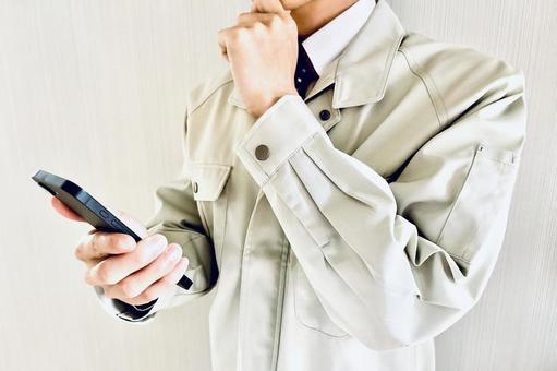 スマホを見て悩む作業着姿の男性 男性,ビジネスマン,疑問の写真素材