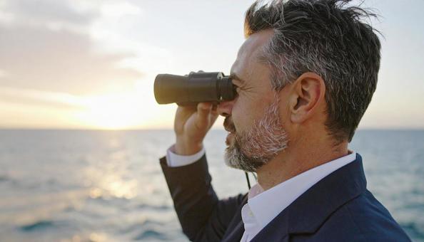 双眼鏡で海の先を見ている男性 双眼鏡で海の先を見ている男性の写真
