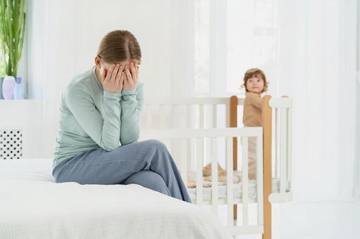 両手で顔を覆いベッドに座る女性 両手で顔を覆いベッドに座る女性 育児疲れ,顔を覆う,泣くの写真素材