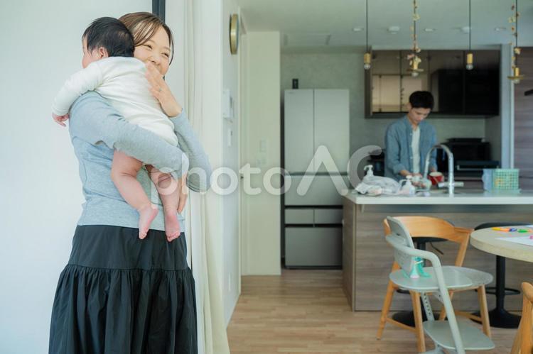赤ちゃんを抱っこするママとキッチンのパパ 赤ちゃん,新生児,母親の写真素材