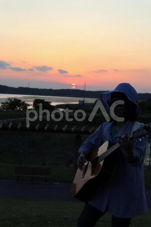 夕陽の前で弾き語り 女性,ギター,夕陽の写真素材