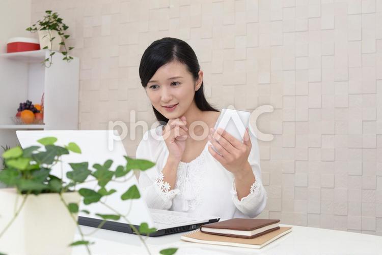 スマホを持ってパソコン作業をする女性 女性,スマホ,ビジネスの写真素材