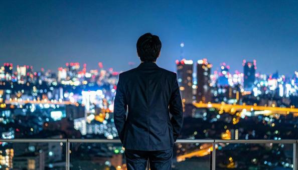 都市の夜景を背景に佇むビジネスマン 都市の夜景を背景に佇むビジネスマンの写真