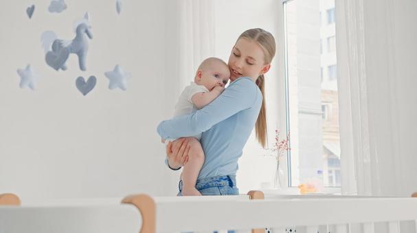 窓際で眠そうな赤ちゃんを抱く長袖の女性 窓際で眠そうな赤ちゃんを抱く長袖の女性 親子,抱っこ,赤ちゃんの写真素材