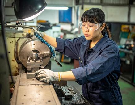 工場で加工機械で金属加工する女性スタッフの写真
