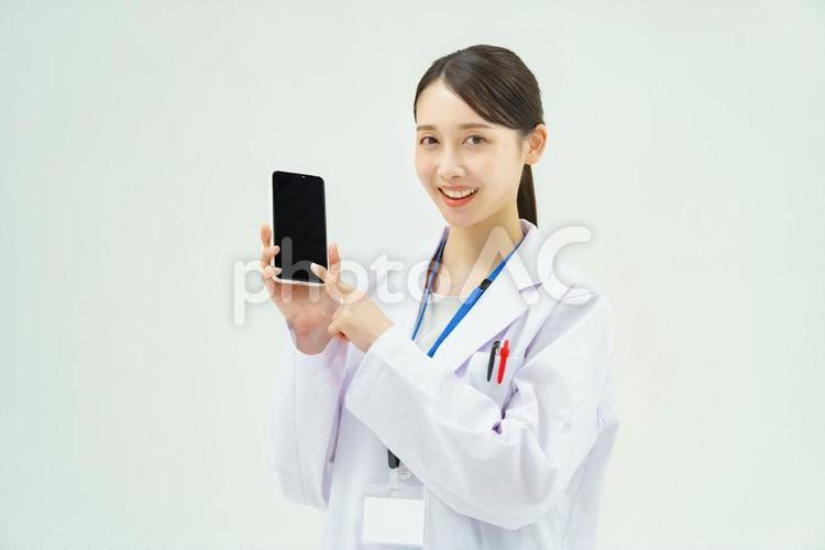 スマートフォンの画面を見せる白衣の女性 医師,医者,スマホの写真素材