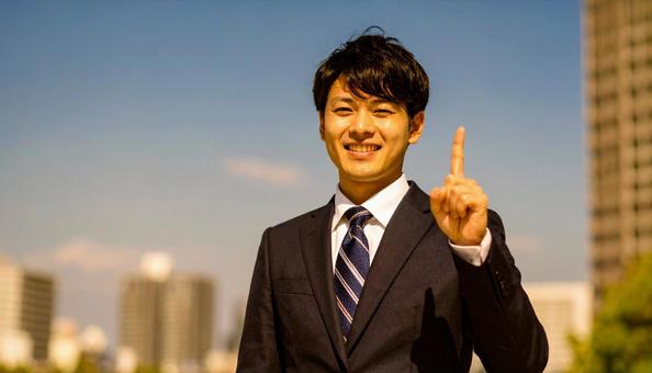 都市背景で人差し指を立てるビジネスマンの写真