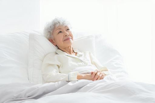 ベッドで寝ているシニア女性 ベッドで寝ているシニア女性の写真