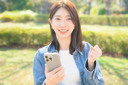 スマホを持ってガッツポーズをする女性 スマホを持ってガッツポーズをする女性の写真