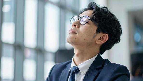 疲れて空を見上げる日本人のサラリーマンの写真