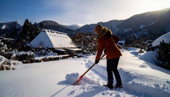 大雪が降った日の翌日の朝に雪かきする女性 大雪が降った日の翌日の朝に雪かきする女性の写真