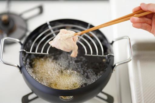 揚げる前の鶏肉を菜箸で持つ人の手の写真