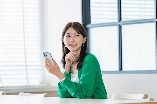 室内でスマートフォンを持ち微笑む女性 室内でスマートフォンを持ち微笑む女性 女性,スマートフォン,携帯電話の写真素材