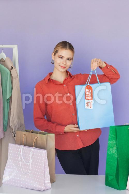 セールのタグの付いたハンガーに掛かった洋服と紙袋を持っている白人女性 セール,ショップ,女性の写真素材