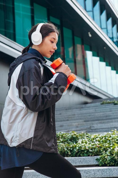 階段で真剣にダンベルを持って筋トレする女性 女性,ヘッドフォン,筋トレの写真素材