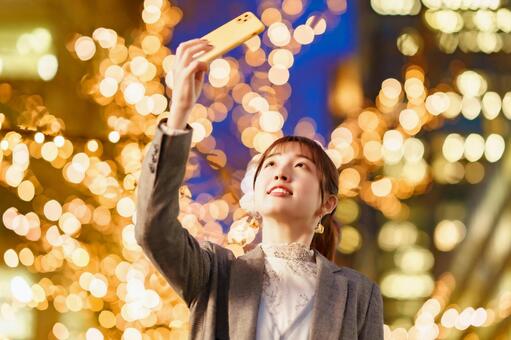 イルミネーションが輝く街で写真を撮る女性  女性,イルミネーション,女子大生の写真素材