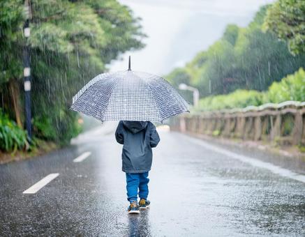 雨の日に傘をさして道路を歩く男の子の写真