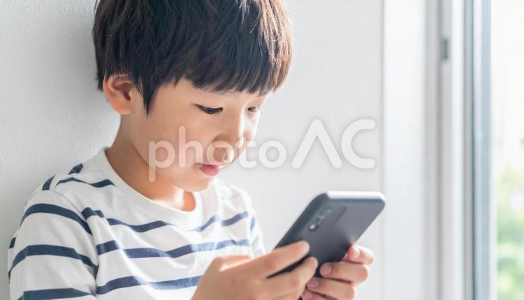 スマホを操作する小学生のこども こども,男の子,スマホの写真素材