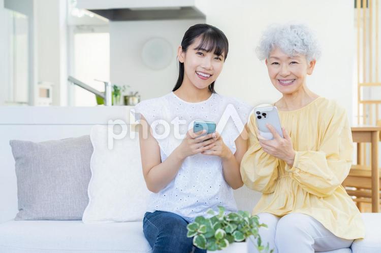 リビングスマホを見てくつろぐ孫と祖母 家族,シニア,女性の写真素材