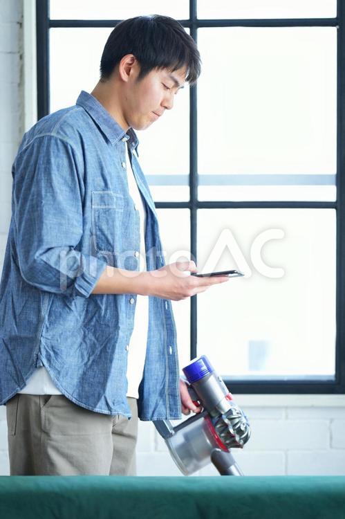 携帯を持って掃除する男性 男性,リビング,ソファーの写真素材