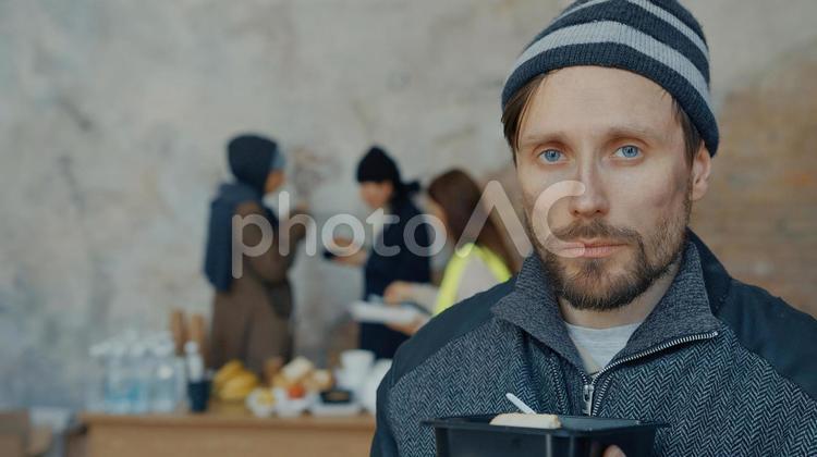 食べ物を持った男性と後ろで炊き出しする人 男性,ニット帽,人物の写真素材