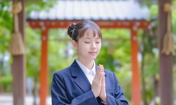 神社で手を合わせる制服姿の女性の写真