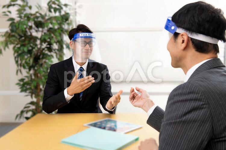 オフィスでフェイスシールドをして打ち合わせをする会社員 フェイスシールド,会社員,男性の写真素材