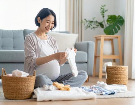 ベビー服を畳みながら微笑む妊婦の準備時間 ベビー服を畳みながら微笑む妊婦の準備時間の写真