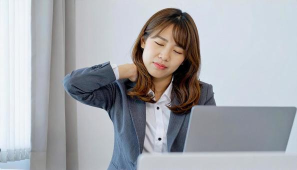 デスクワーク中に肩こりに悩む女性社員 デスクワーク中に肩こりに悩む女性社員の写真
