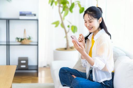 部屋でスマホを操作する女性 スマホ,笑顔,部屋の写真素材