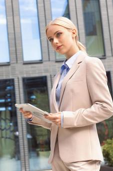 オフィスビルの外でタブレットを持って立っているスーツの女性 ビジネスウーマン,ビジネス,女性の写真素材