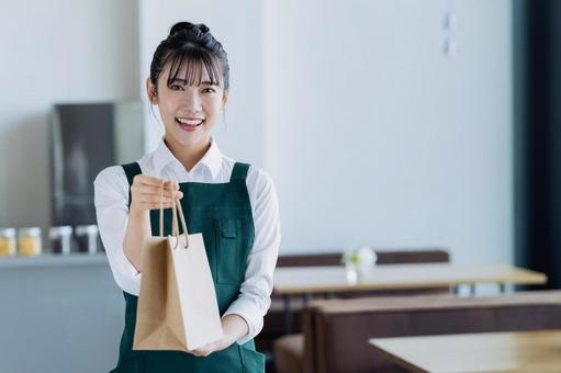 紙袋を渡す若い女性の店員 紙袋を渡す若い女性の店員の写真