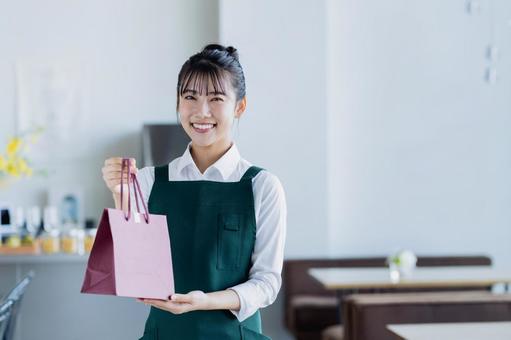 紙袋を渡す若い女性の店員 紙袋を渡す若い女性の店員の写真