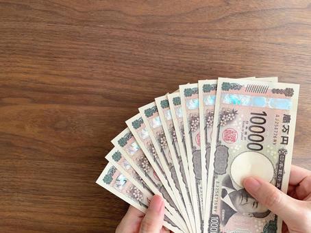 A woman's hand holding 100,000 yen on a desk, JPG A woman's hand holding 100,000 yen on a desk, JPG