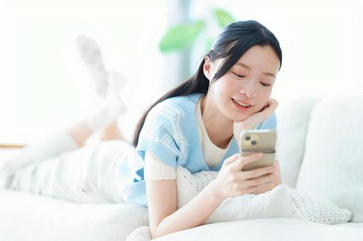 ソファに寝転びスマホを見る女性 女性,スマートフォン,持つの写真素材