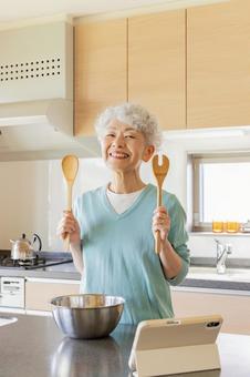 タブレットを見ながら料理するシニア女性 キッチン,タブレット,料理の写真素材
