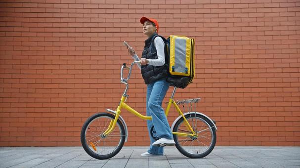 自転車にまたがってスマートフォンを使っているフードデリバリーの女性 配達,フードデリバリー,デリバリーの写真素材