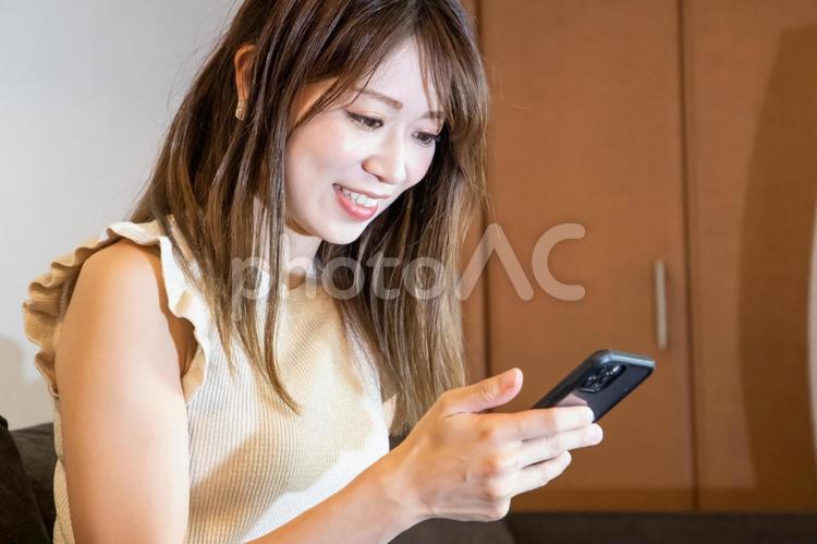 ソファーに座りスマホを見る笑顔の女性 女性,笑顔,微笑みの写真素材