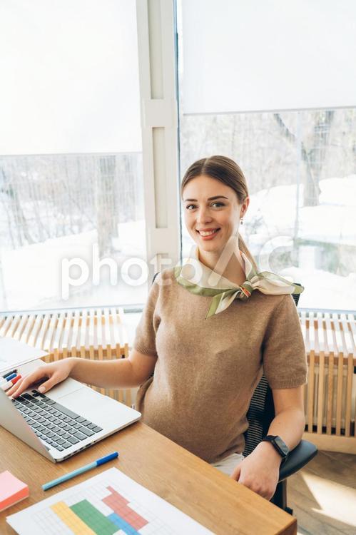 オフィスでデスクワークするカメラ目線の妊娠中の女性 ビジネス,ビジネスウーマン,女性の写真素材