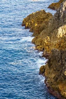 青い海と岩礁に打ち付ける白い波の写真