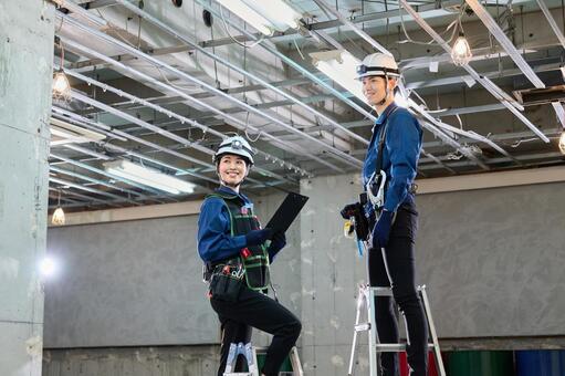 脚立に乗って現場点検する男女作業員2人 作業員,工事現場,電気工事の写真素材