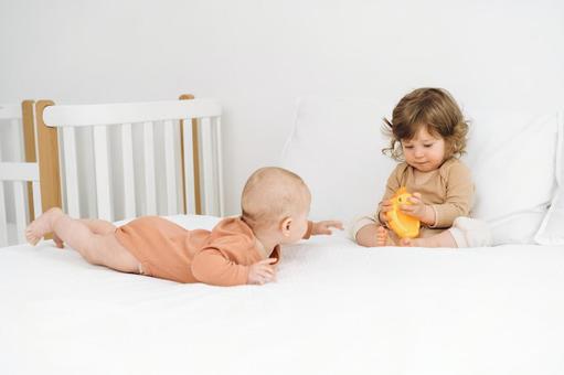 座っている子供が持つ玩具が気になる赤ちゃん 座っている子供が持つ玩具が気になる赤ちゃん 赤ちゃん,かわいい,ベッドの写真素材