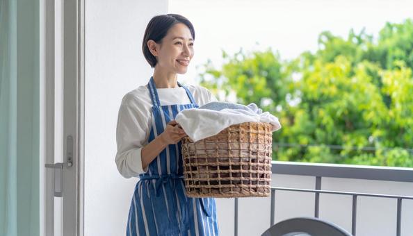 洗濯物が入った籠を抱えるエプロンの女性 洗濯物が入った籠を抱えるエプロンの女性の写真