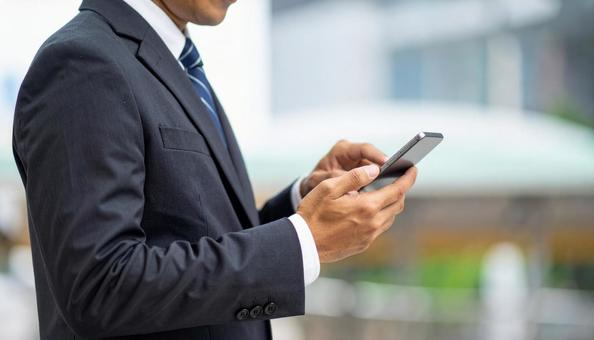 屋外でスマホを操作するビジネスマンの手元の写真