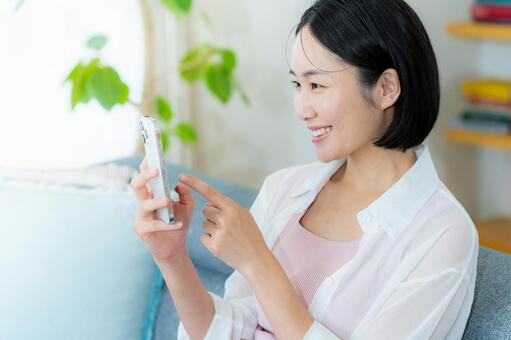 部屋でスマホを操作する女性 スマホ,笑顔,部屋の写真素材