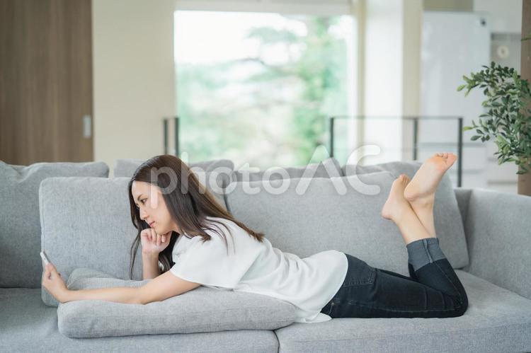 ソファでスマホを使う女性（考える） スマホ,女性,困るの写真素材