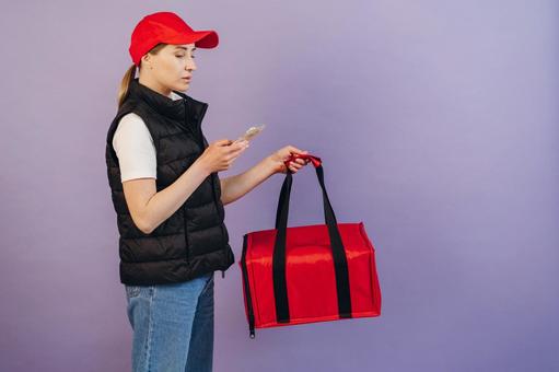 保温ピザバッグを持ってスマートフォンを使う女性配達員 配達,フードデリバリー,デリバリーの写真素材