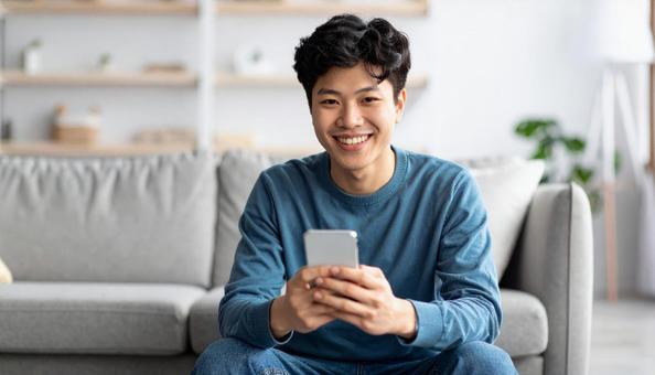 スマホを手に笑顔の男性の室内ポートレートの写真