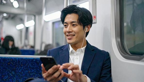 電車に座って携帯電話を見るビジネスマン 電車に座って携帯電話を見るビジネスマンの写真