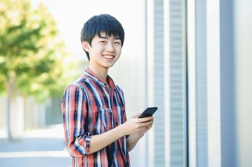 スマホを持ってほほえむアジア人の男子学生 スマホを持ってほほえむアジア人の男子学生の写真